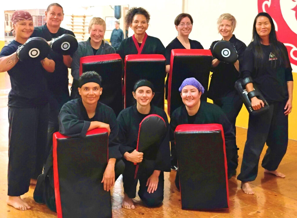 LGBTQIA+ Self Defense Class - Photo of four smiling people holding pads and other martial arts equipment